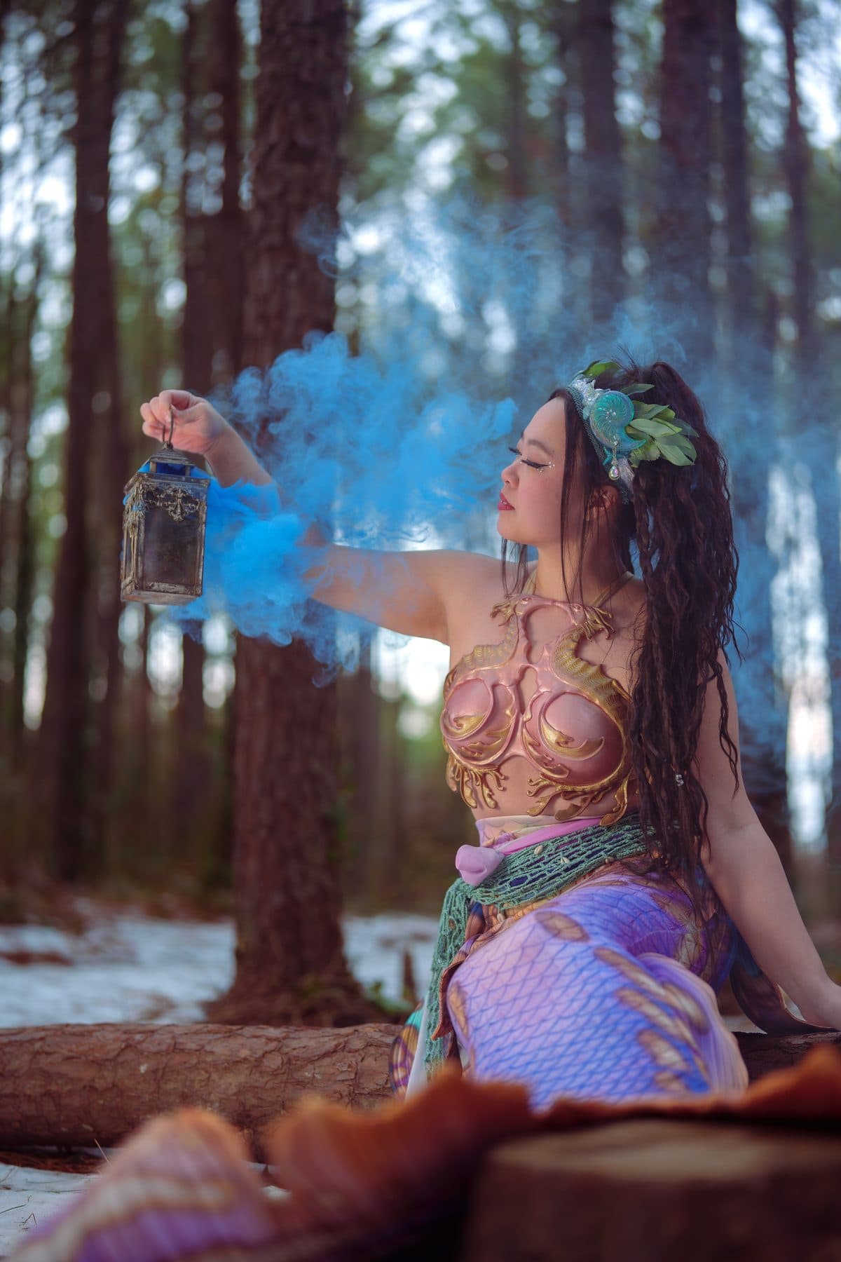 Mermaid Ro holding a lantern among woodland greenery and cyan smoke